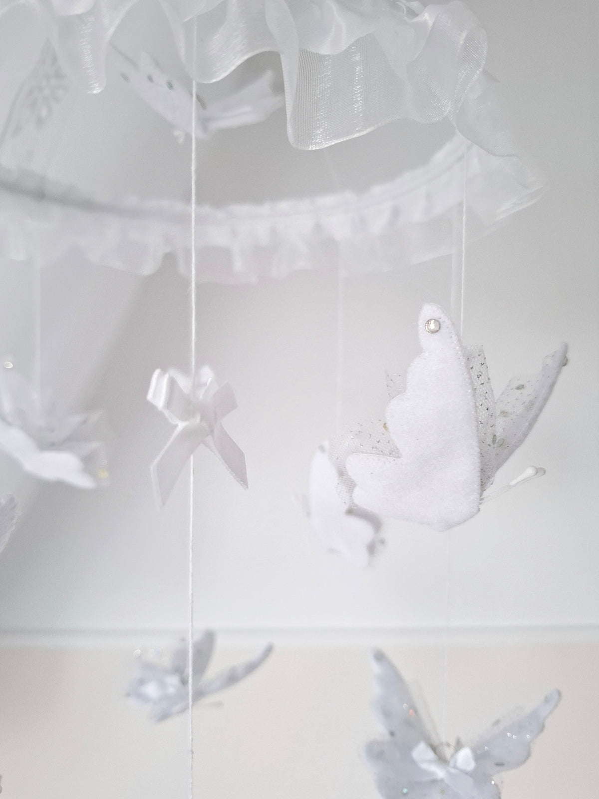White-on-white baby mobile with soft butterflies and sheer ruffles, adding gentle elegance to a serene nursery design.

