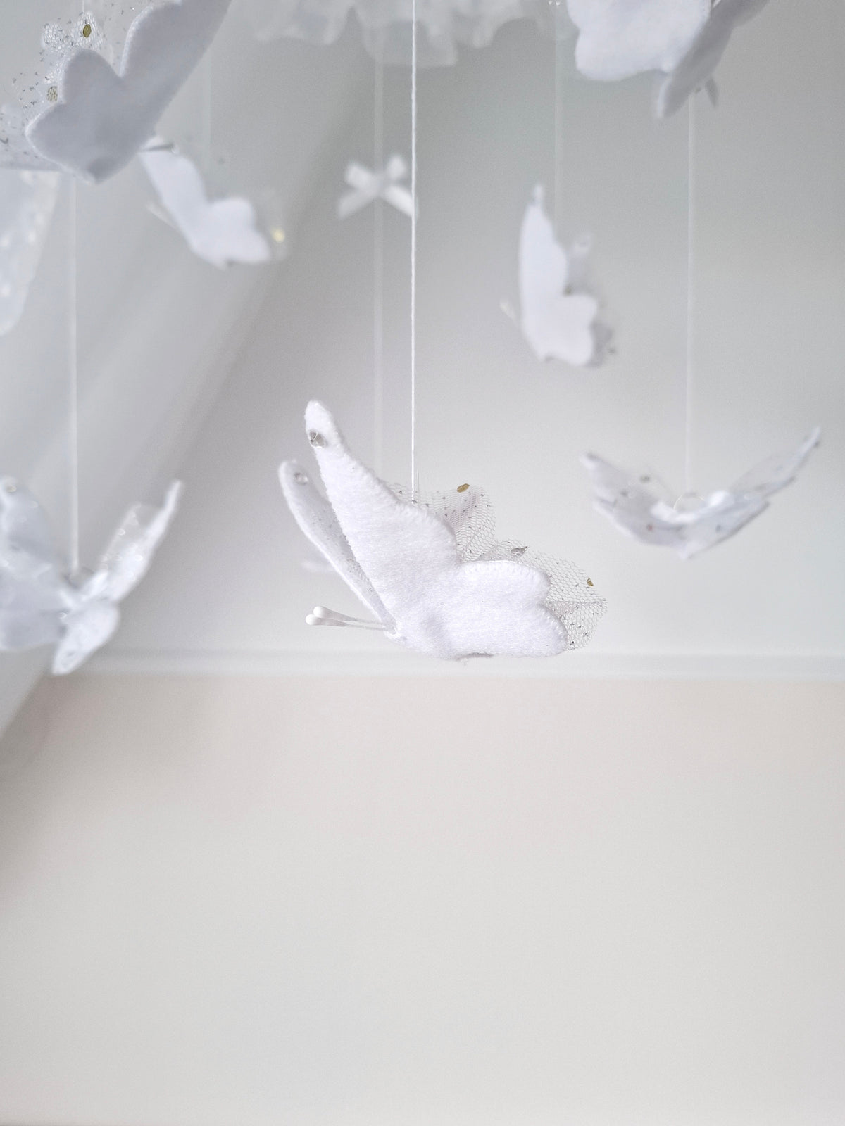 Ethereal butterfly mobile in all white with floating felt shapes and airy ruffled details, ideal for a minimalist, luxurious nursery.