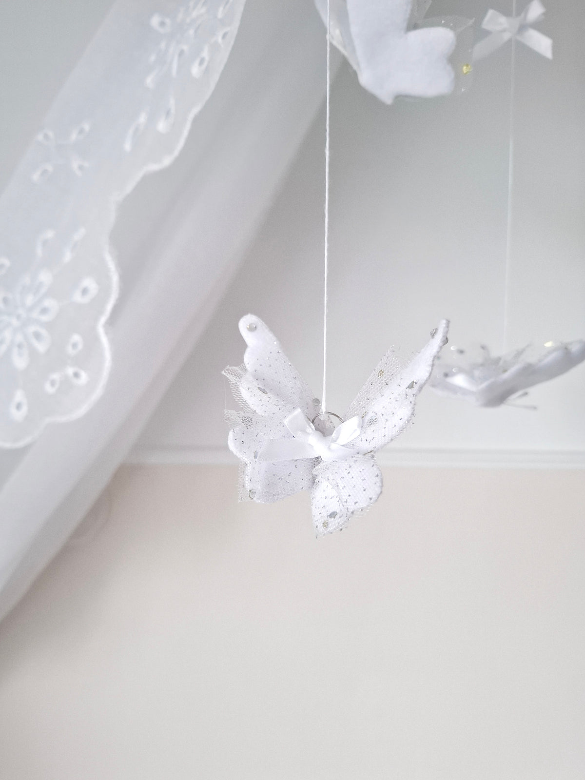 Handmade baby mobile with soft white butterflies and lace accents, designed to flutter gently above the crib in dreamy stillness.