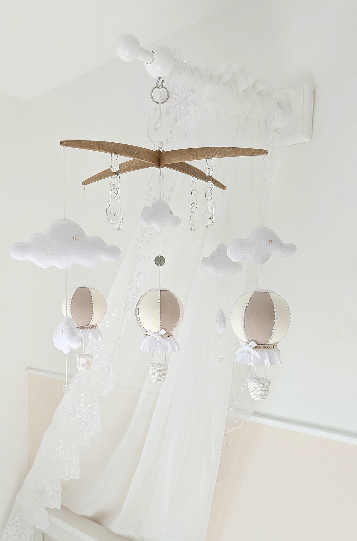 Luxury balloon mobile in soft neutrals with felt clouds and crystal drops, hanging above a pale nursery cot.