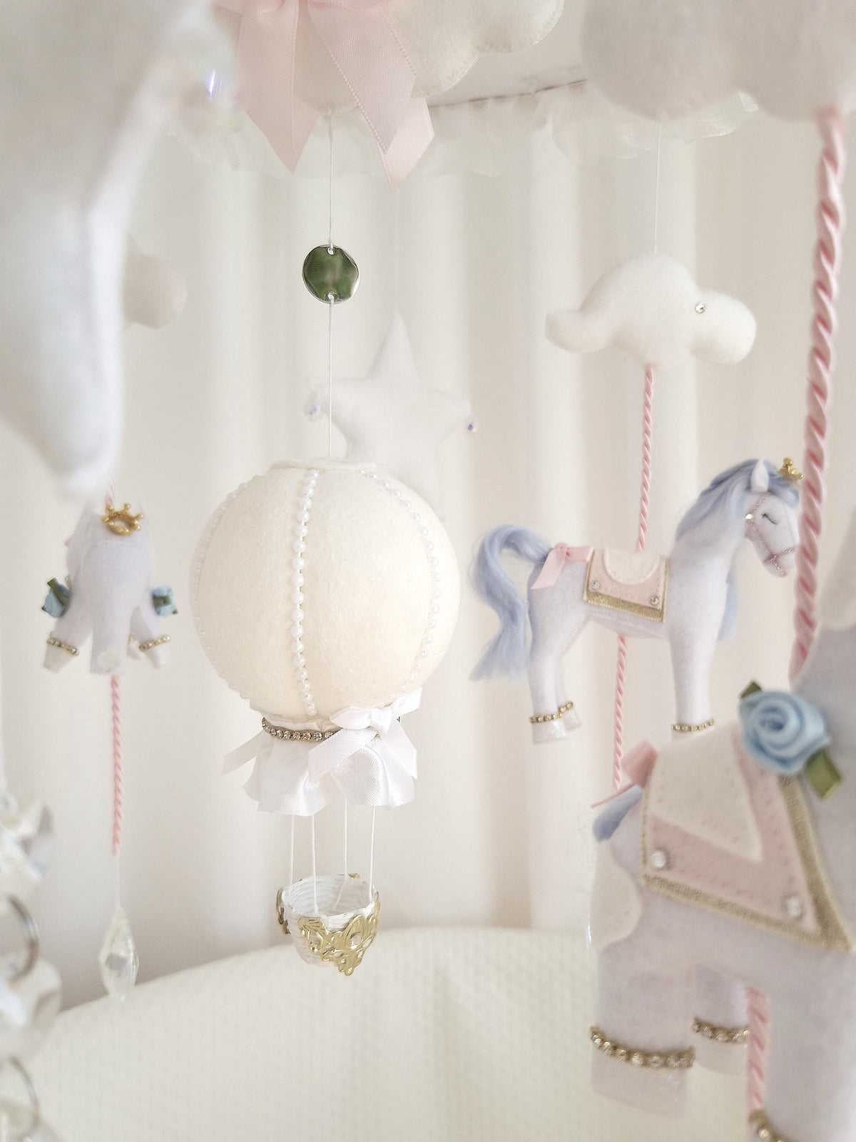Rear view of the handmade felt carousel horse showing the blush pink saddle, blue tail and gold decorative trim.