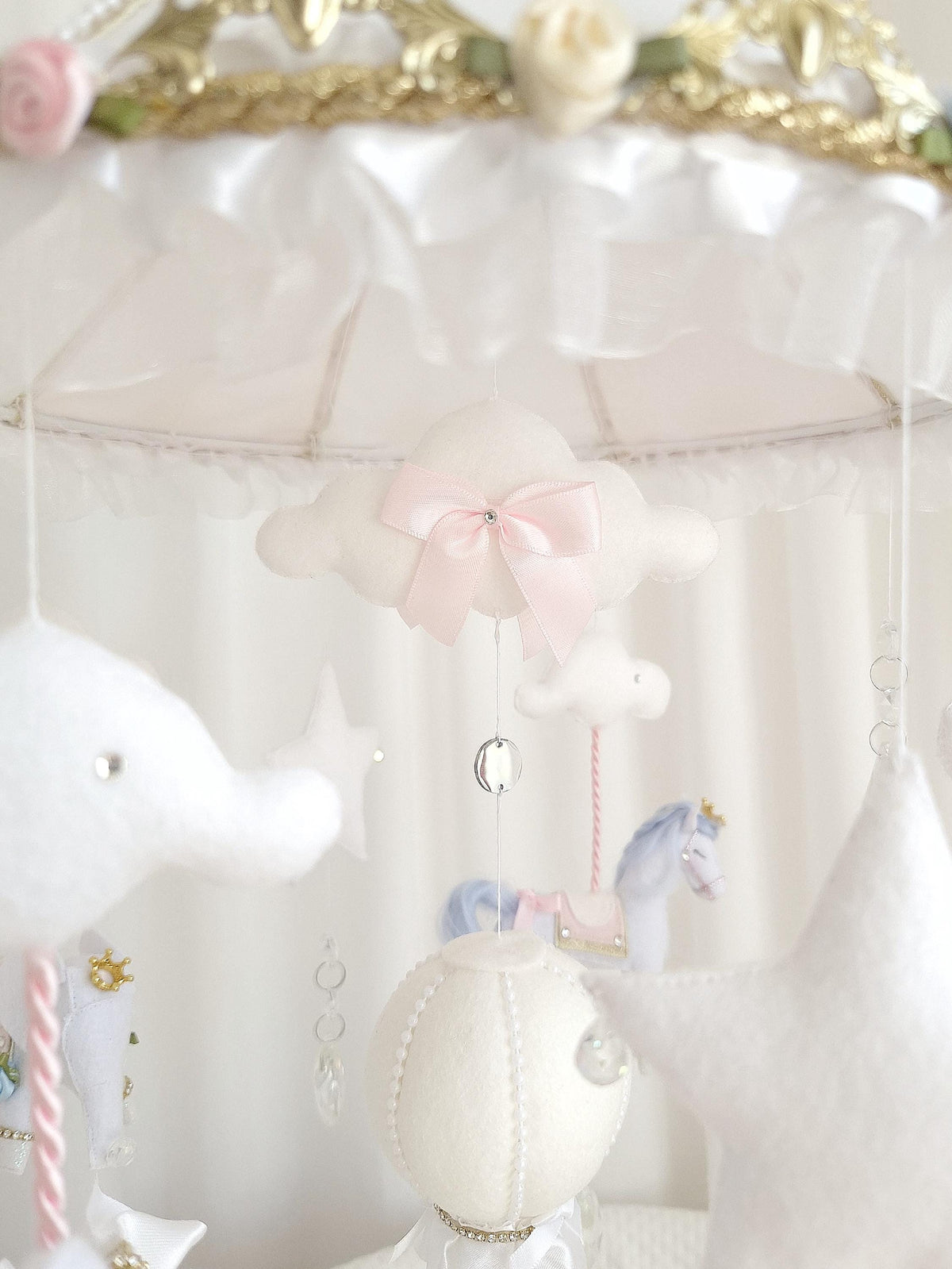 Close-up of the top of the handmade hot air balloon showing a blush pink bow, ruffle trim and hanging clouds.