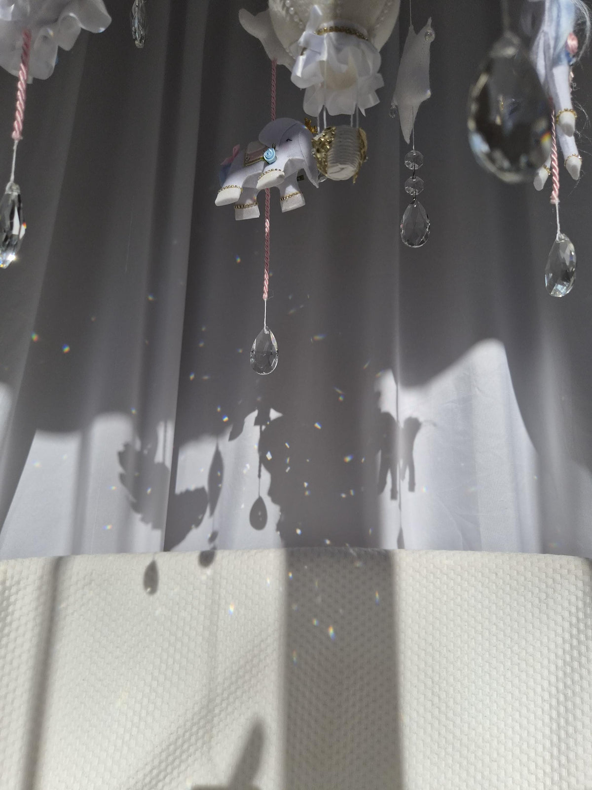 Glass crystal hanging beneath the carousel baby mobile creating sparkling rainbow reflections in natural sunlight.