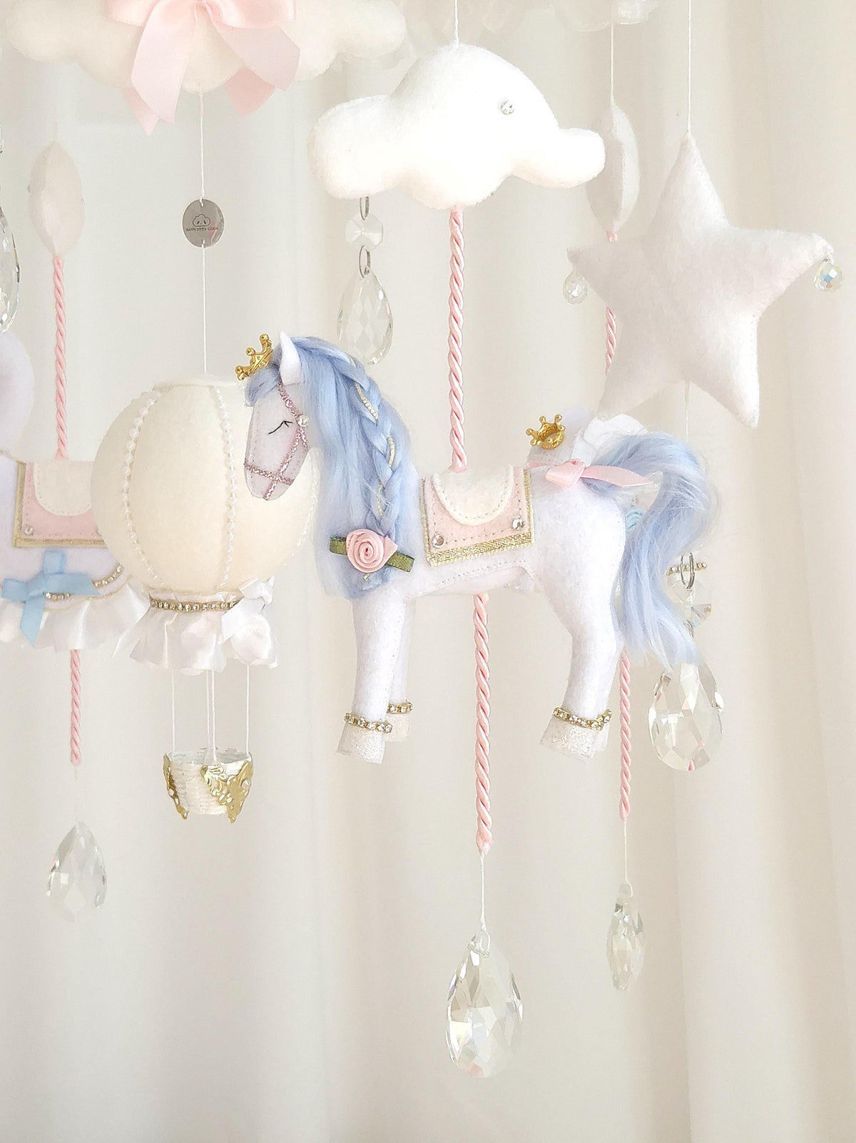 Front view of a handmade carousel baby mobile with crowned swans, horses, elephants, stars, clouds and glass crystal accents in white, blush pink and blue.