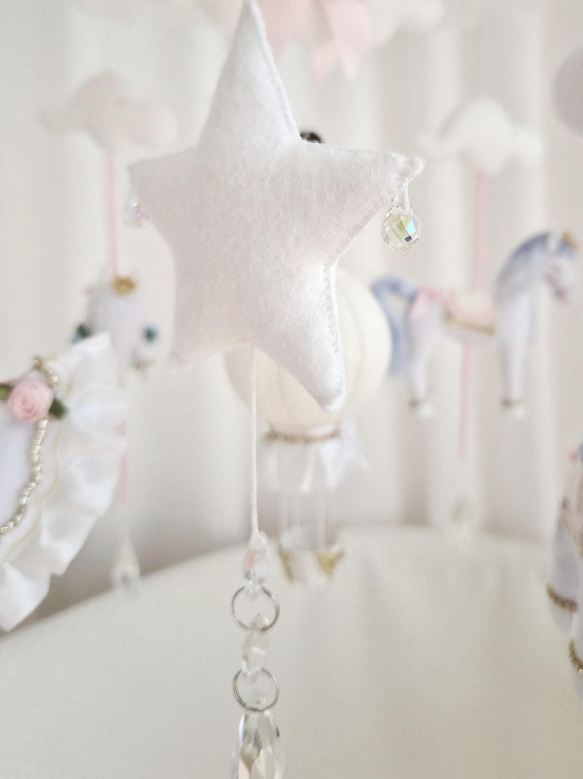 Close-up of a handmade felt star with a hanging glass crystal beneath it on the carousel nursery mobile.
