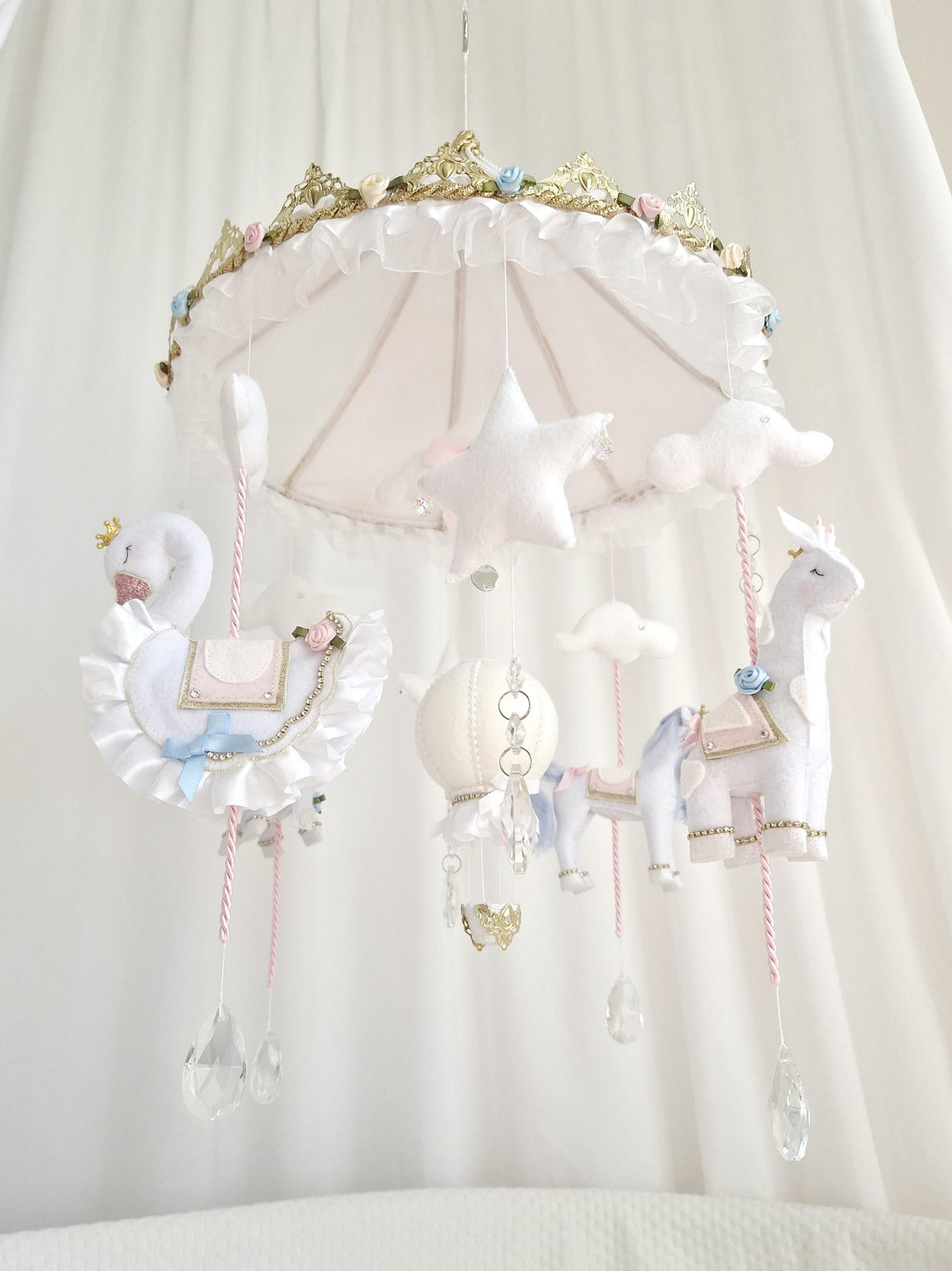 Side view of a handmade carousel nursery mobile with felt animals, hot air balloons and crystal decorations hanging from a decorative gold carousel canopy.