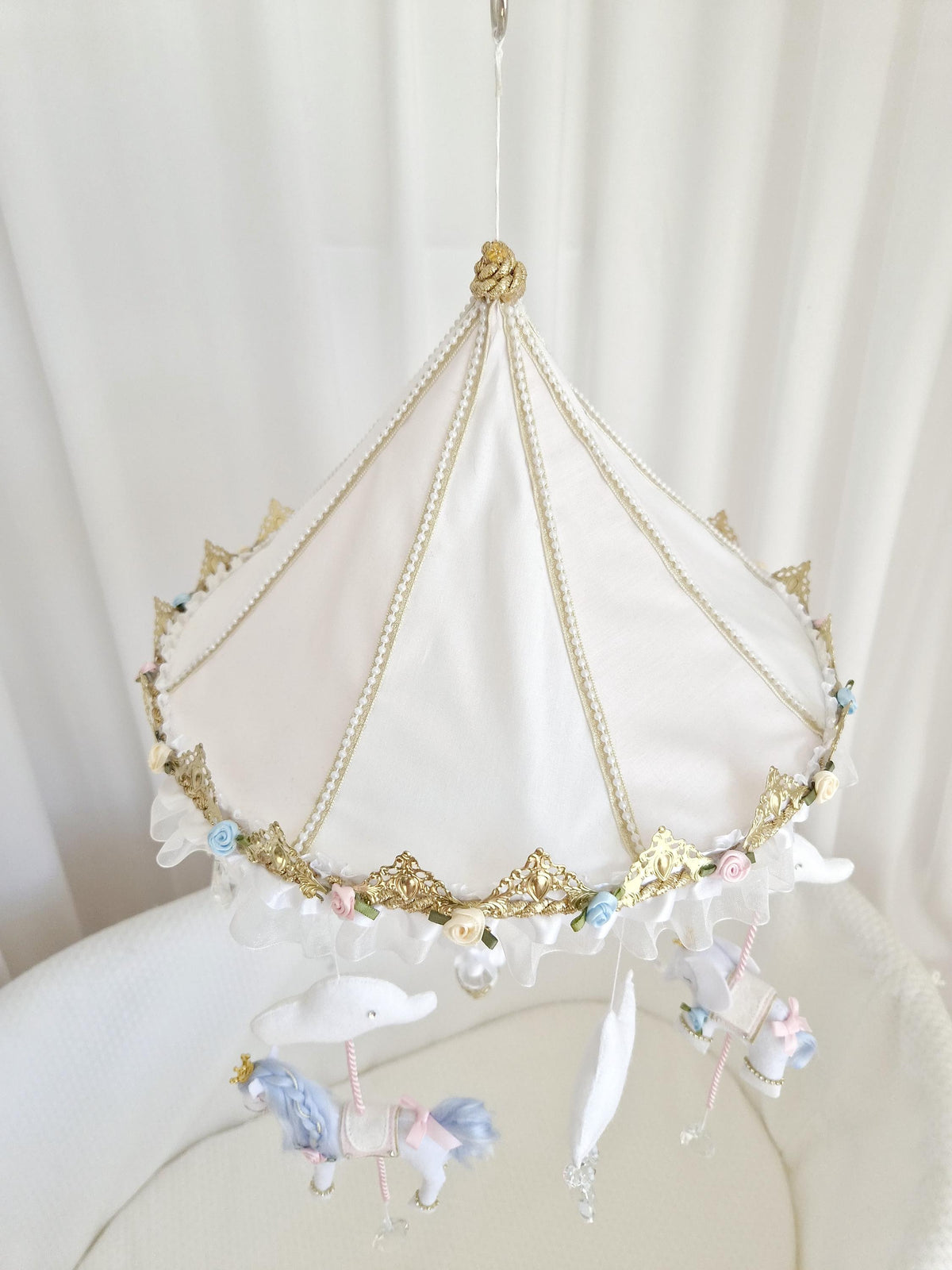 Decorative gold and white carousel canopy with floral embellishments supporting the handmade felt baby mobile.