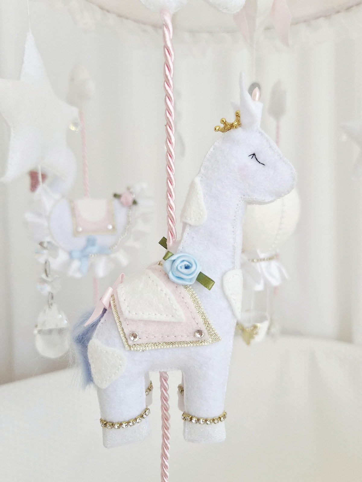 Rear view of the handmade felt carousel horse showing the blush pink saddle, blue tail and gold decorative trim.