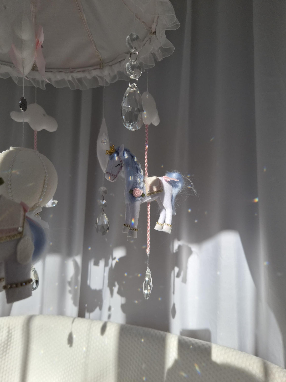 Handmade carousel nursery mobile hanging in warm natural sunlight with shimmering crystal reflections in a neutral nursery.