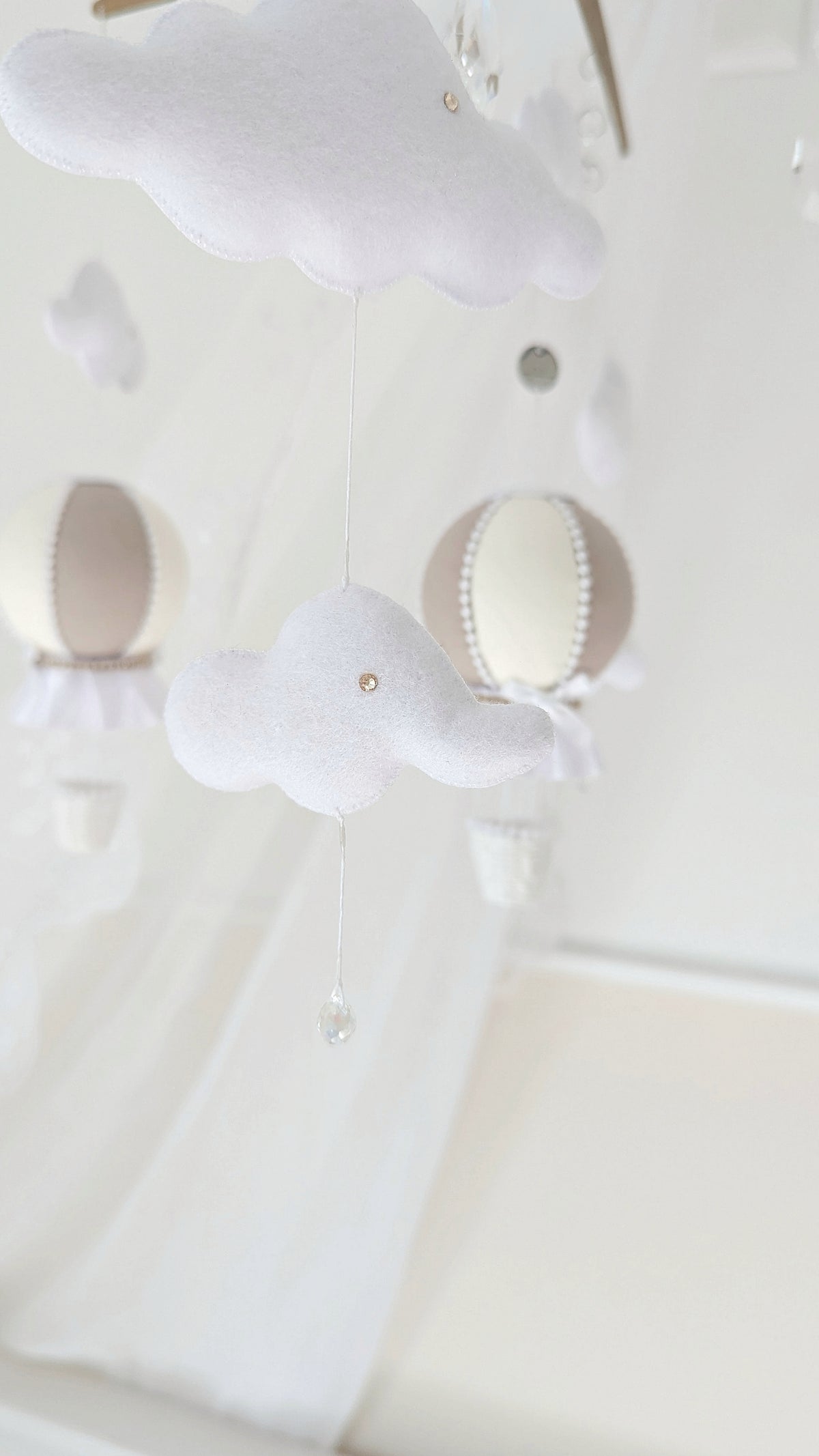 Handmade baby mobile with cloud and balloon elements, hung from a wooden cross frame with sparkling crystal accents.

