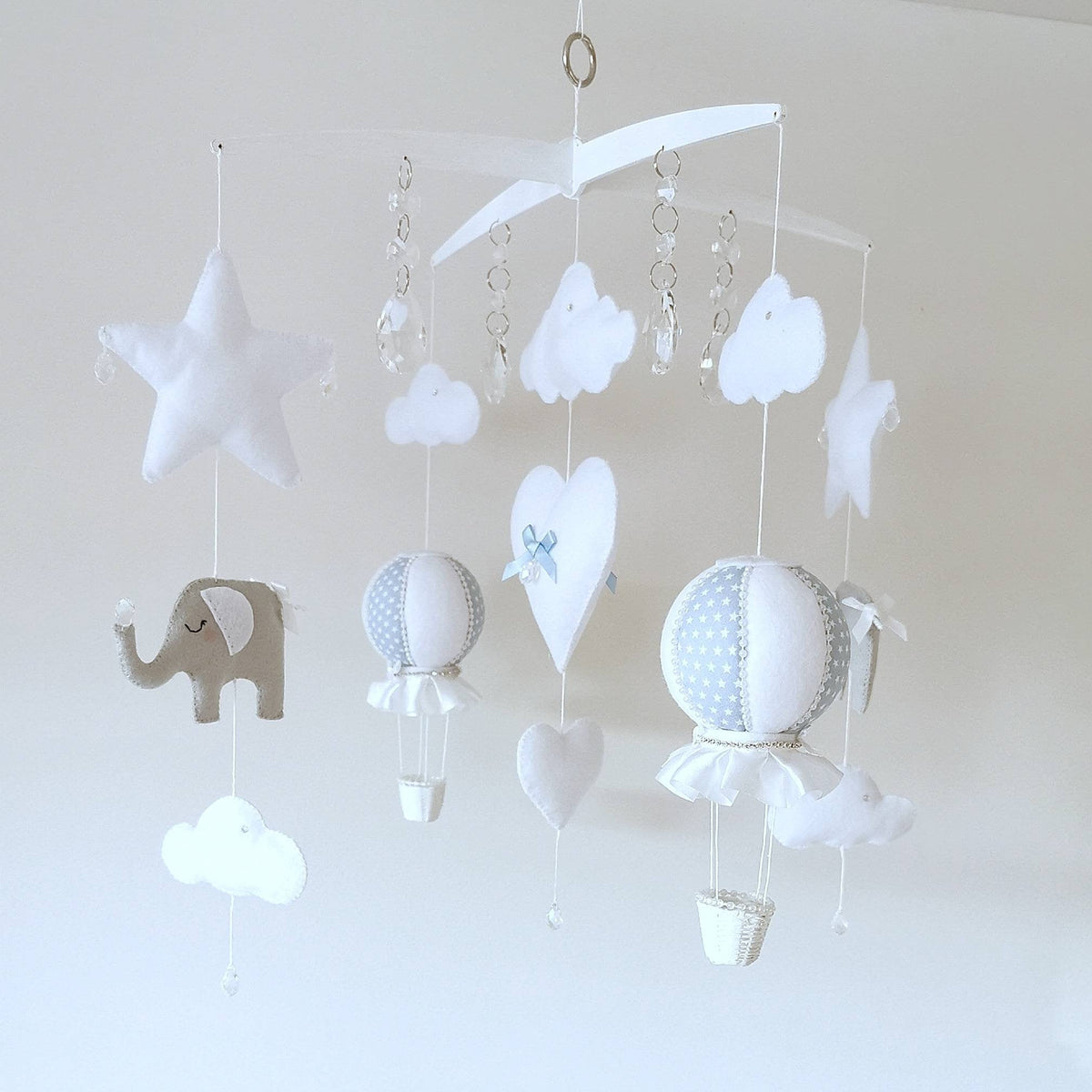Close up of soft blue and white hot air balloons with delicate stitching, clouds, stars and  waving elephant below.
