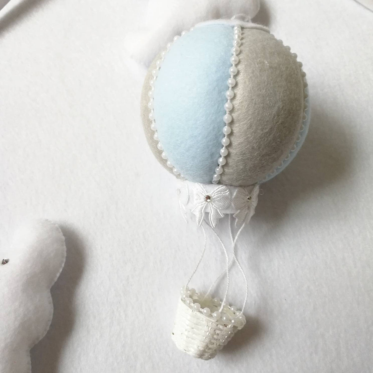 Close up of a handmade pale blue felt hot air balloon with tiny white basket, part of a baby mobile.
