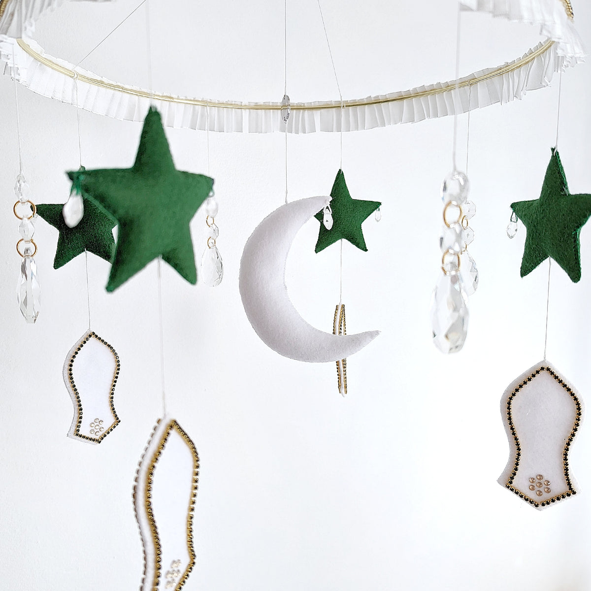 Crescent moon mobile with green stars, mosque shapes, and a felt sandal detail symbolising the Prophet Muhammad’s (pbuh) footsteps.

