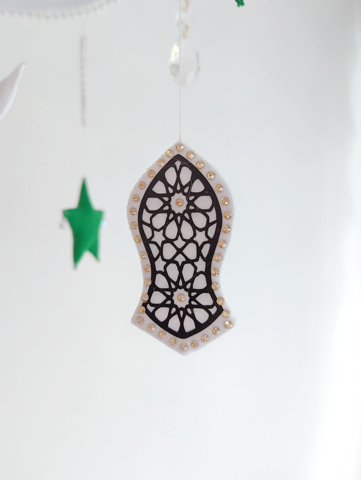 Crescent moon baby mobile featuring deep green stars and intricate sandal symbols, inspired by Islamic tradition.

