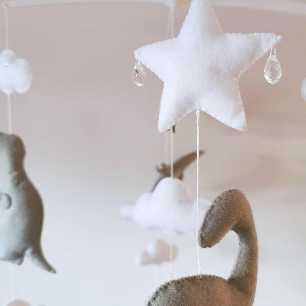 Playful nursery mobile featuring dinosaurs floating among stars and clouds in soft, neutral tones.