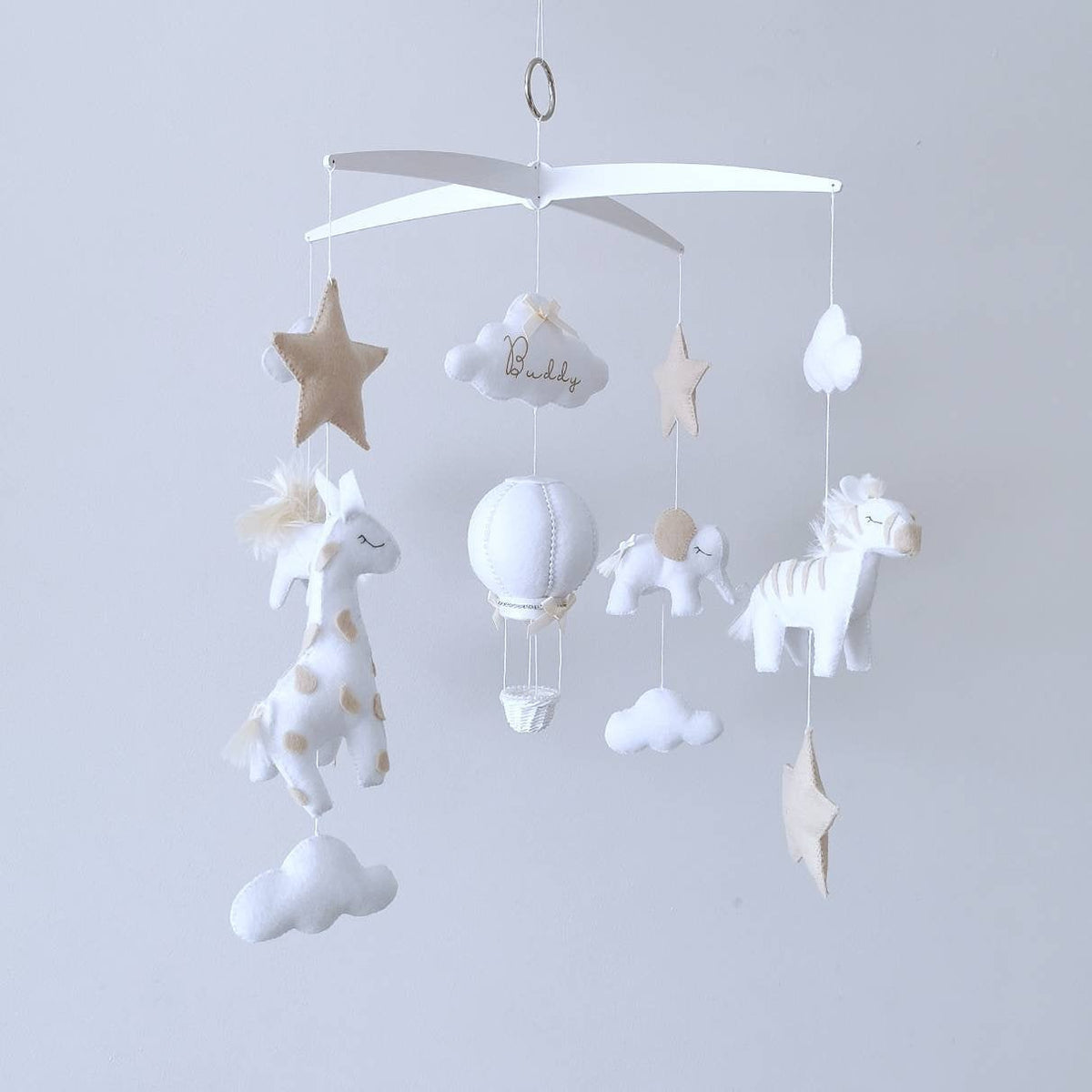Close-up of handcrafted felt lion with fluffy mane, part of a neutral safari baby mobile, luxury animal-themed nursery detail.

