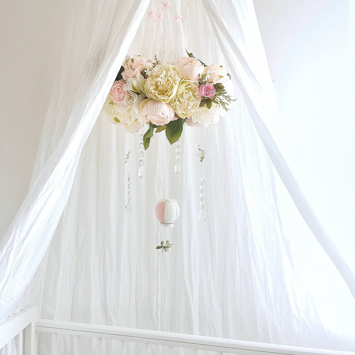 Baby mobile with a garden-style floral ring in blush and cream tones, accented by crystals and leaves.
