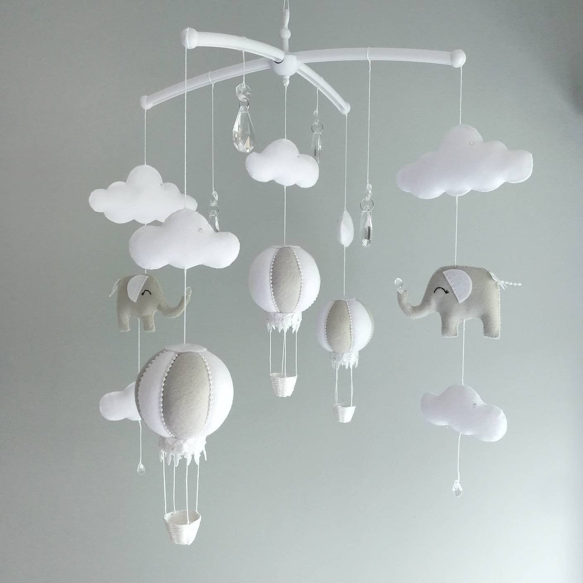 Handmade baby mobile with soft grey hot air balloons, gentle elephants, and fluffy clouds floating together in a peaceful neutral palette.