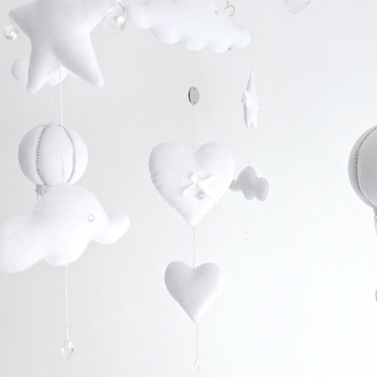 Handmade baby mobile with floating hot air balloons and cloud elements, creating a peaceful, airy scene above the cot.

