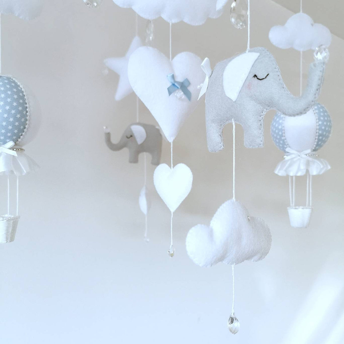 Heirloom nursery mobile with soft felt elephants, stitched hearts, and hot air balloons in gentle blue and grey.

