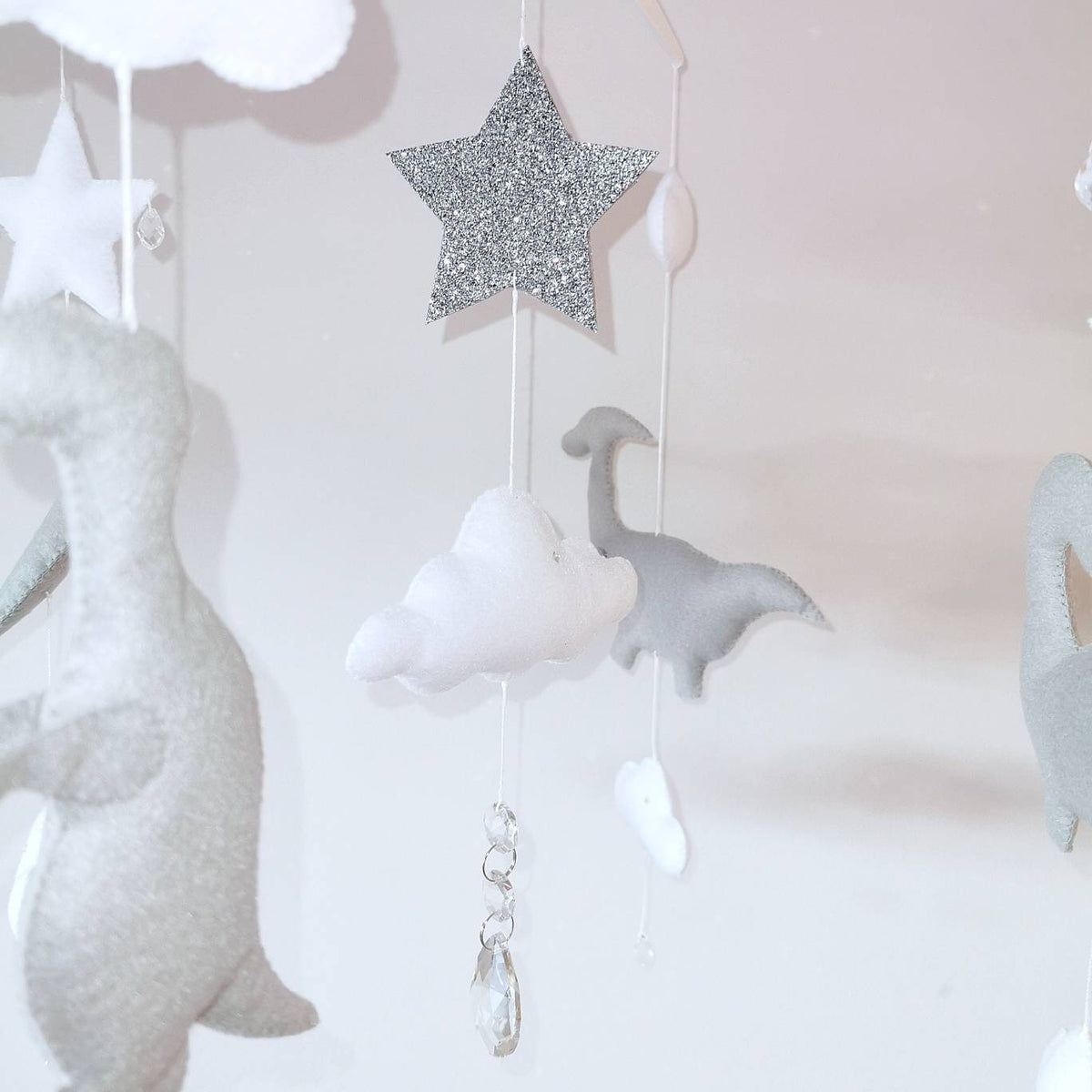 Luxury felt mobile with gentle clouds, sparkling star, and handcrafted dinosaurs floating in a dreamy scene.