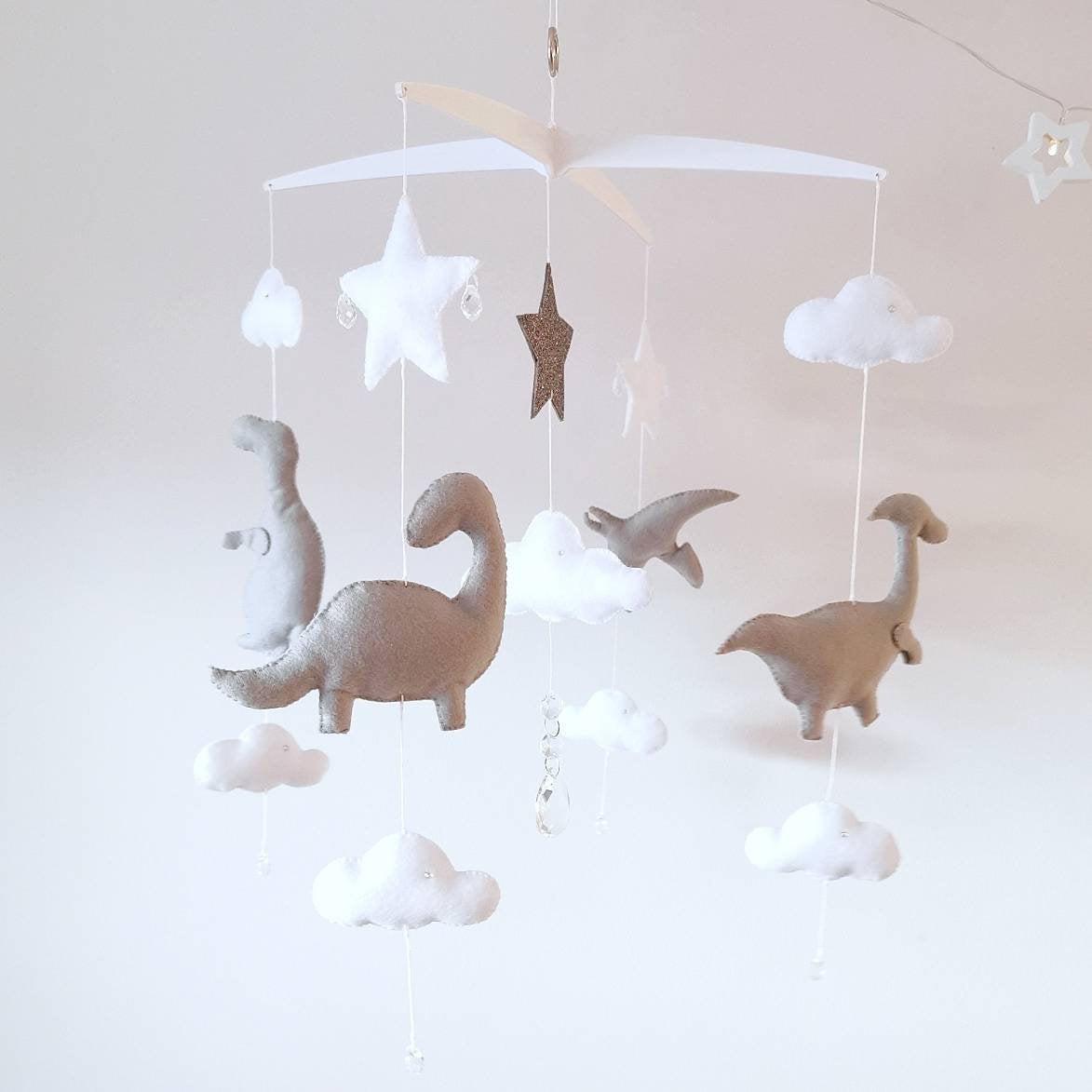 Neutral dinosaur-themed baby mobile with soft grey dinos, white clouds, and stars hanging from a cross-style hanger.

