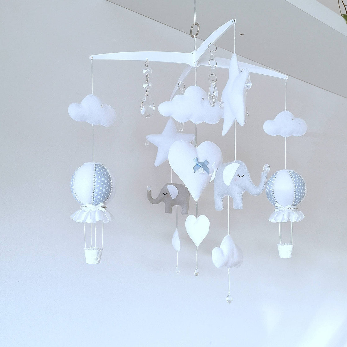 Luxury baby mobile with soft elephants, fluffy clouds, and blue polka dot hot air balloons on a white cross-style hanger.