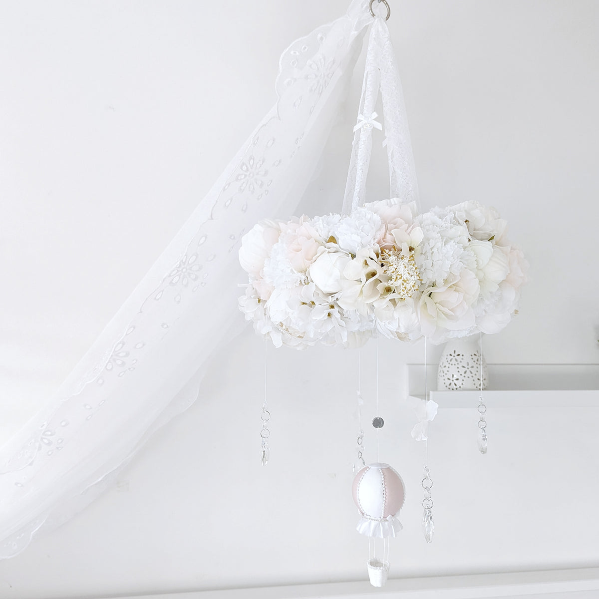Elegant baby mobile with a lush floral wreath and a single blush pink hot air balloon, styled in a soft white nursery.