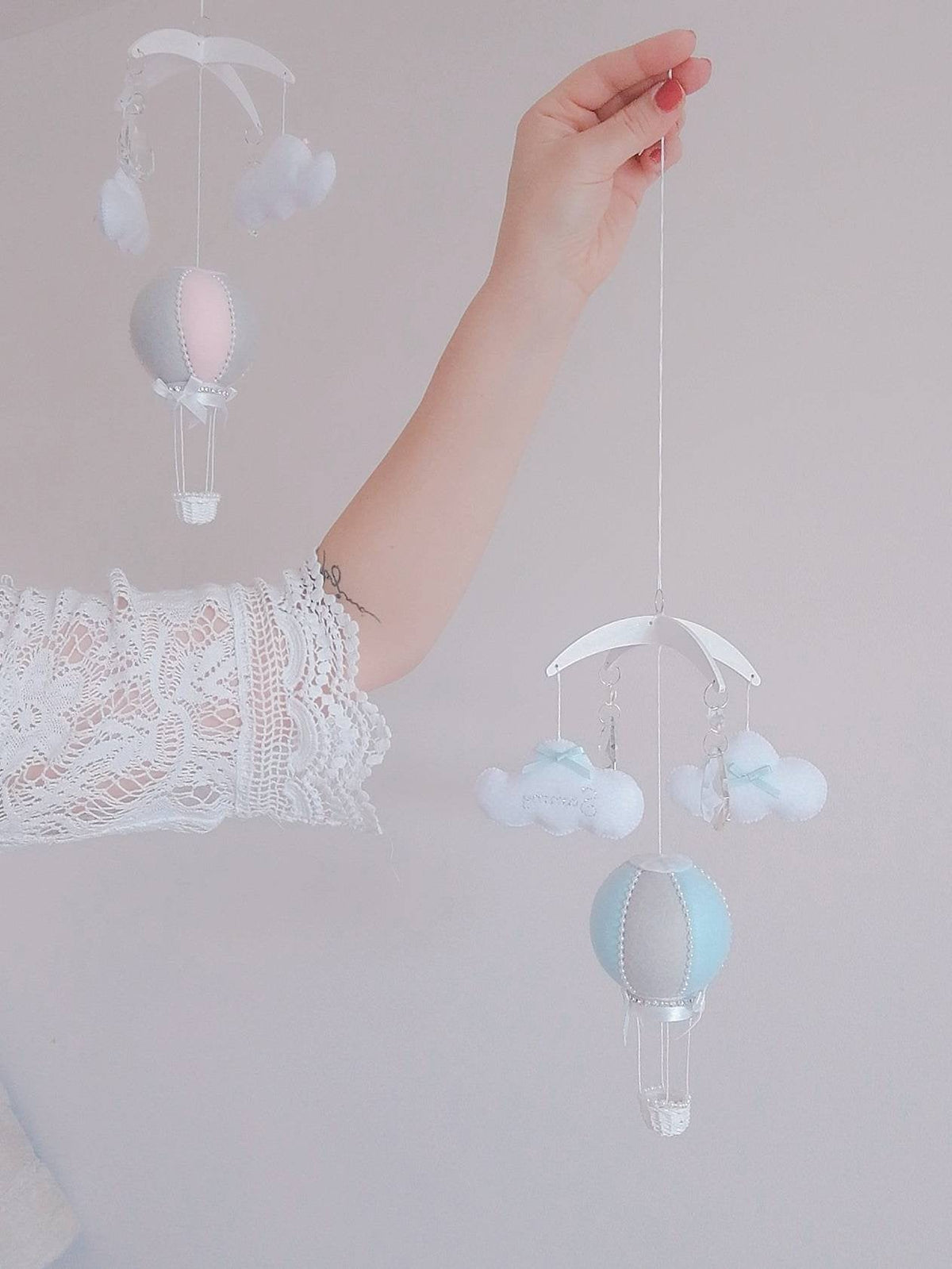 Mini hot air balloon baby mobile in soft blue and ivory with hanging clouds, shown held in hand, perfect for moses basket or bassinet. Baby shower, christening or birth gift

