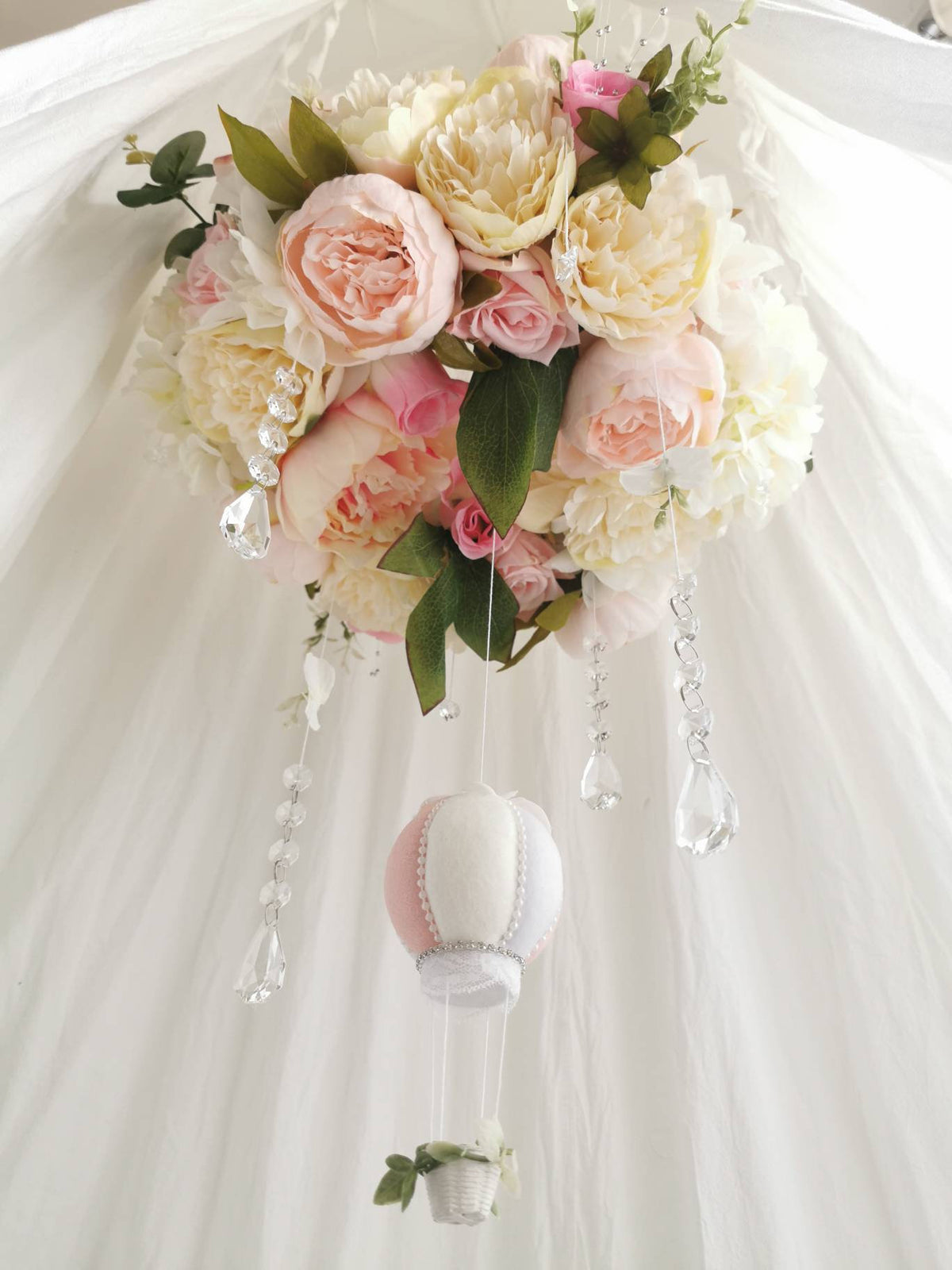 Close-up of soft blush-toned florals and sparkling hanging crystals on an heirloom-quality baby mobile.

