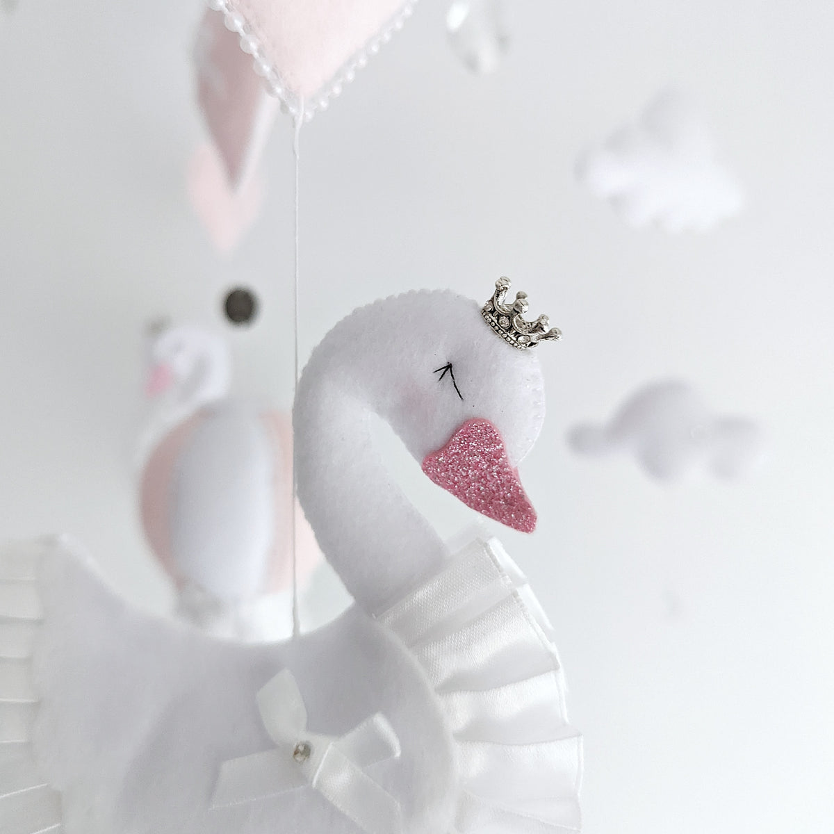 Detailed view of sparkling crystal droplets and soft felt hearts in blush and white, ethereal accents for a luxury handmade swan nursery wall charm.

